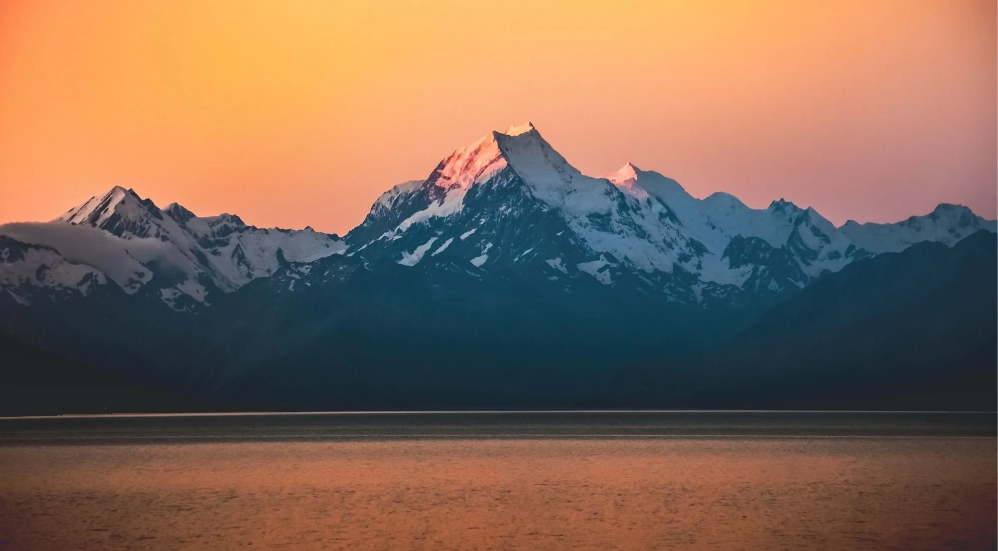 Aoraki/Mount Cook catching pink alpenglow under an orange sunset sky