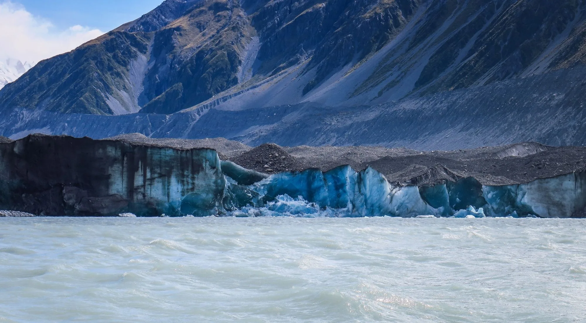 The grey-blue terminal face of a glacier above its meltwater lake