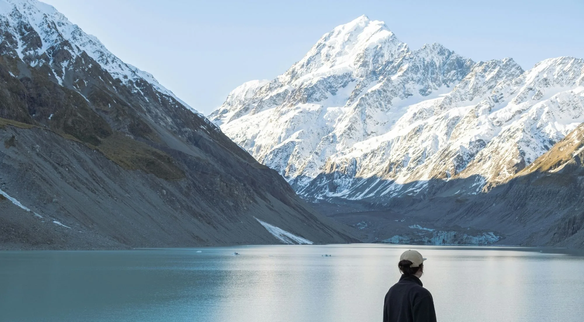 Walker looking across a glacier lake towards Aoraki/Mount Cook